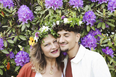 Smiling mother and son wearing tiaras against flower plants at back yard during swedish summer solstice