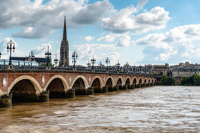 Arch bridge over river by buildings against sky