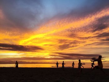 Silhouette of people on beach against cloudy sky