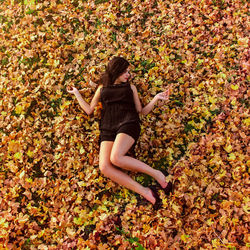 High angle view of young woman lying on leaves covered field