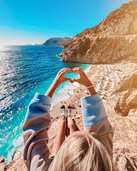 Rear view of woman sitting at beach against sky