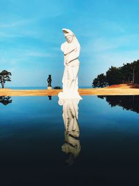 Digital composite image of statue by lake against sky