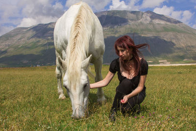 Woman with white horse on field against mountain