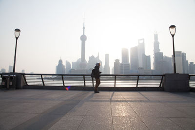 Side view of woman on sidewalk against city skyline