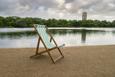 Empty chair on lake against sky