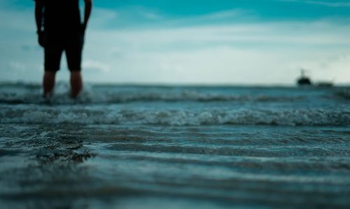 Midsection of man standing in sea against sky during sunset