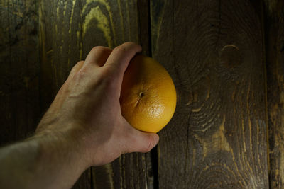 Cropped hand of man holding orange on wooden table