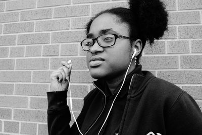 Young woman looking away while listening music through headphones against brick wall