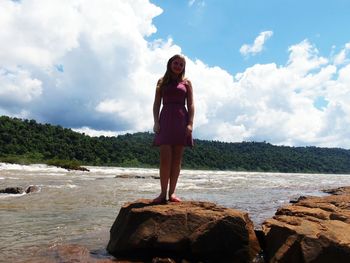 Low angle view of young woman standing on rock against river