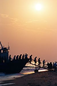 Silhouette people on beach against sky during sunset
