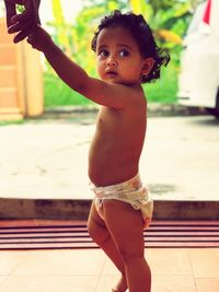 Side view of shirtless cute baby girl looking away while standing on floor