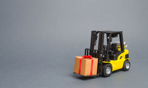 Yellow forklift truck carries a gift with a red bow. purchase and delivery of a present.