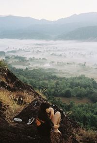 Rear view of woman sitting on mountain against sky