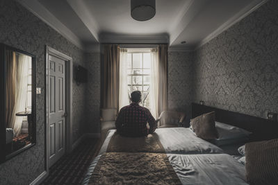 Rear view of man sitting on bed at home