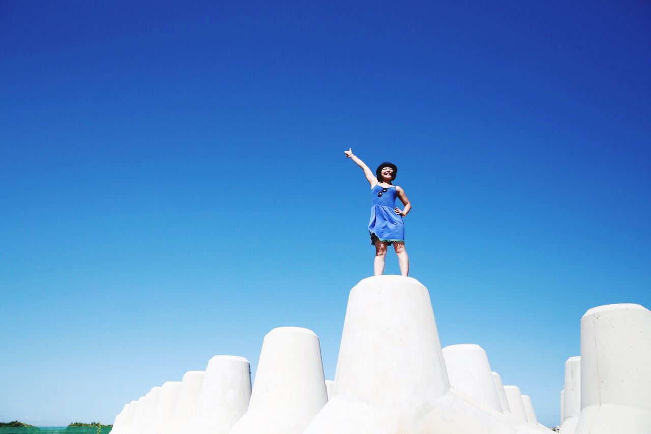 blue, clear sky, low angle view, copy space, leisure activity, standing, carefree, full length, casual clothing, enjoyment, day, getting away from it all, vacations, young adult, stone material, creativity