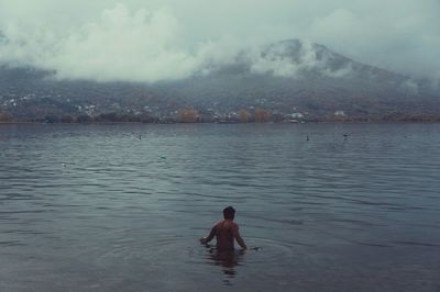 Rear view of man swimming in lake against mountain