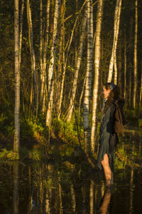 Side view of woman standing in lake against trees at forest