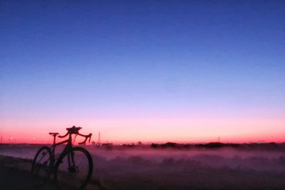 Silhouette bicycle on field against clear sky at sunset