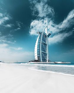 View of modern buildings at beach against cloudy sky