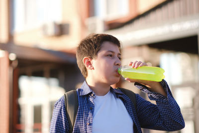 A cute fasion student boy is drinking a bottle of drink outdoor.