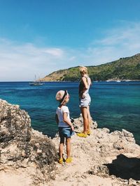 Friends standing on rock by sea against sky