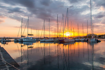 Sailboats moored at harbor against sky during sunset