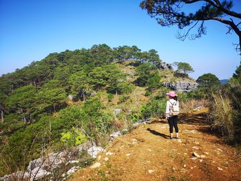 Rear view of woman standing by mountain against clear blue sky