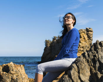 Young woman sitting on rock by sea against sky