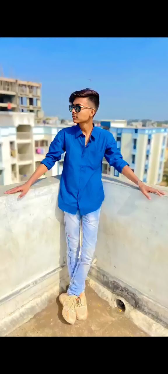 blue, one person, full length, architecture, adult, men, glasses, standing, front view, sunglasses, day, fashion, city, young adult, casual clothing, sky, portrait, leisure activity, outdoors, building exterior, nature, clothing, spring, lifestyles, built structure, sunlight, looking at camera, sports, smiling, transportation, happiness, looking, person, water