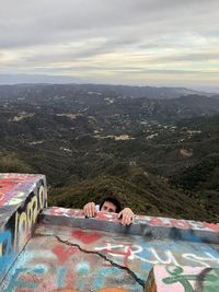 Portrait of young man lying on mountain against sky