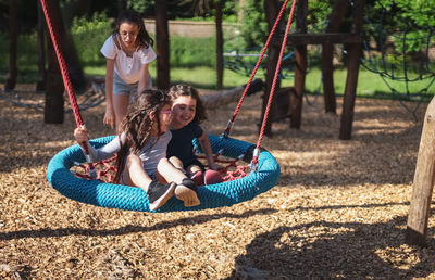 Portrait of a teenage girl pushing her sisters on a round rope swing in the park.