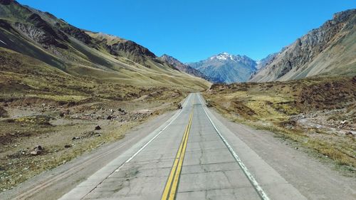 Road leading towards mountains against clear blue sky