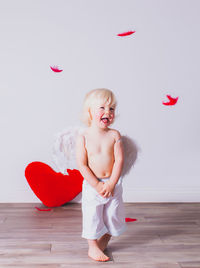 Cute shirtless girl standing on floor against wall