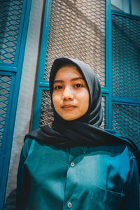 Portrait of young woman standing against window