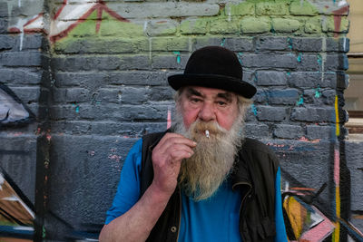 Portrait of man smoking cigarette while standing against wall