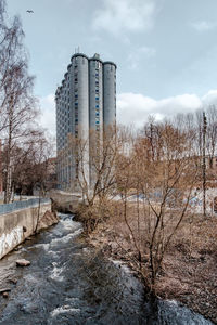 Bare trees by building against sky during winter