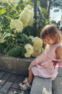 Side view of girl sitting on retaining wall by plants at park