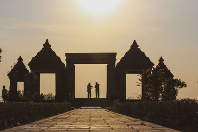 People outside temple against sky during sunset