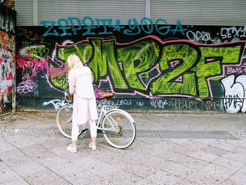 Bicycle parked on sidewalk against graffiti wall