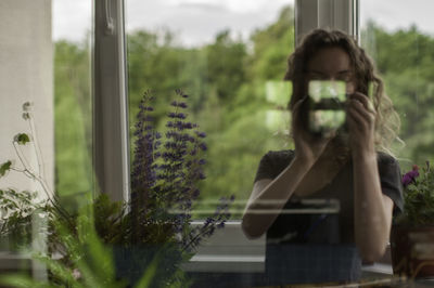 Woman photographing with camera seen through glass window