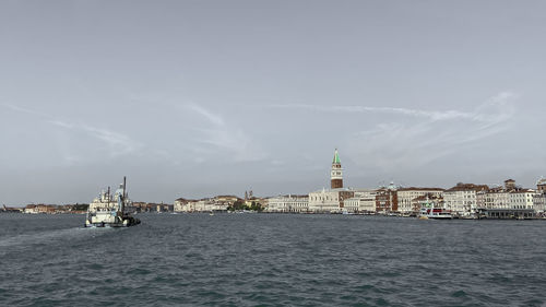 Sailboats in sea by buildings against sky in city
