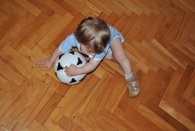 High angle view of boy playing with soccer ball on hardwood floor at home