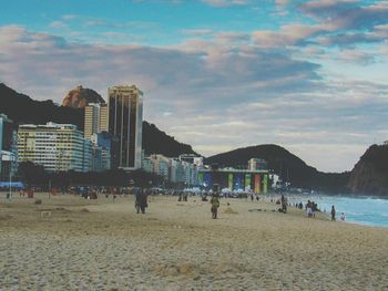 People on beach by city against sky