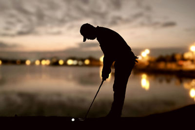 Silhouette man playing golf at sunset