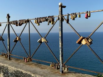 Padlocks on railing by sea against clear sky