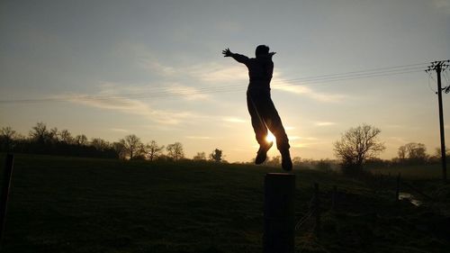 Silhouette man standing on field against sky during sunset