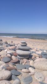 Stacked pebbles at beach against blue sky