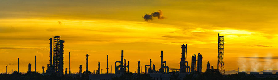 Silhouette factory against sky during sunset