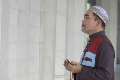 Side view of man with necklace standing in mosque