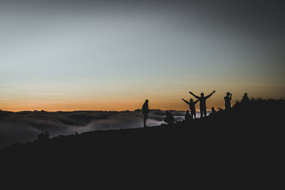 Silhouette people standing on land against sky during sunset